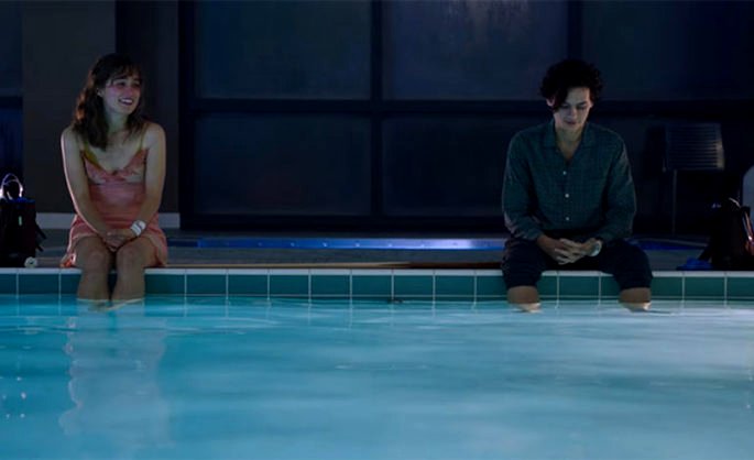 Casal adolescente sentado na beira de uma piscina.