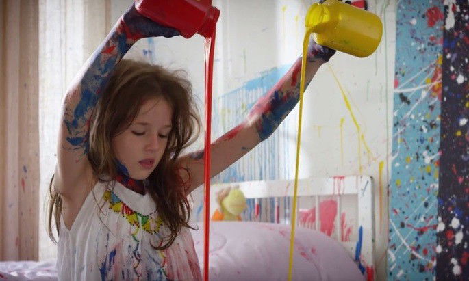 Criança, toda suja de tinta colorida, pintando.