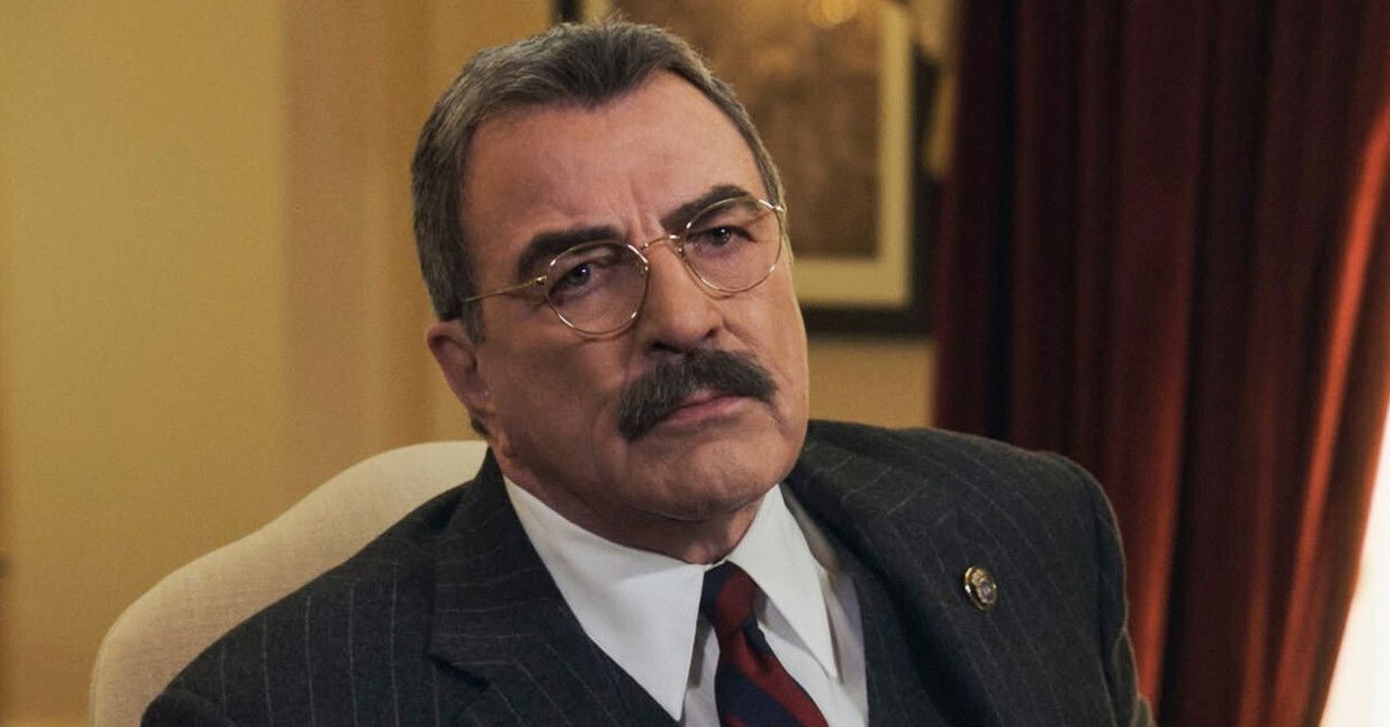 Detetive mais velho, com óculos e bigode, na sua secretária.