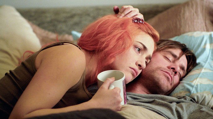 Casal deitado na cama, abraçado, com uma expressão triste.