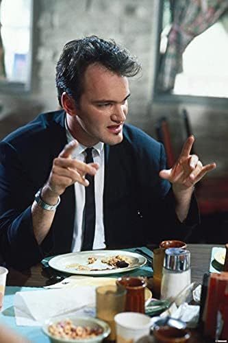 Quentin Tarantino em ação no filme Cães de aluguel, sentado em uma mesa, gesticulando, enquaanto veste terno preto
