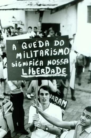 Foto de um protesto de 1968, jovem segura um cartaz pedindo o final do militarismo.