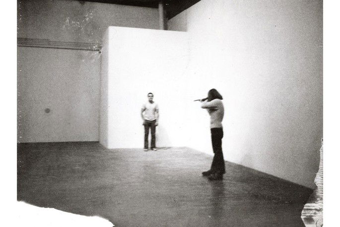 Homem apontando uma arma para outro homem. Performance Shoot, de Chris Burden