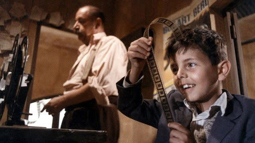 Cena de filme Cinema Paradiso exibe menino olhando negativos de cinema