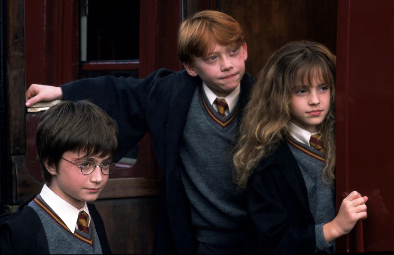 Personagens Rony, Harry Potter e Herminione em pé, na porta vinho de um trem