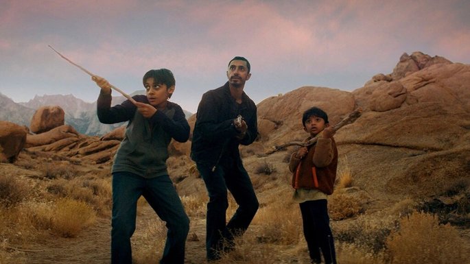 Um homem e dois garotos num local deserto, se protegendo com paus nas mãos.