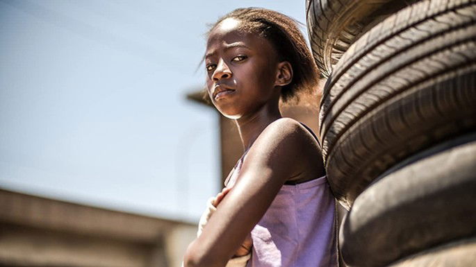 Menina negra vestindo uma blusa rosa e olhando com uma expressão de desconfiança.