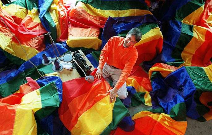 Gilbert Baker rodeado de bandeiras LGBT.