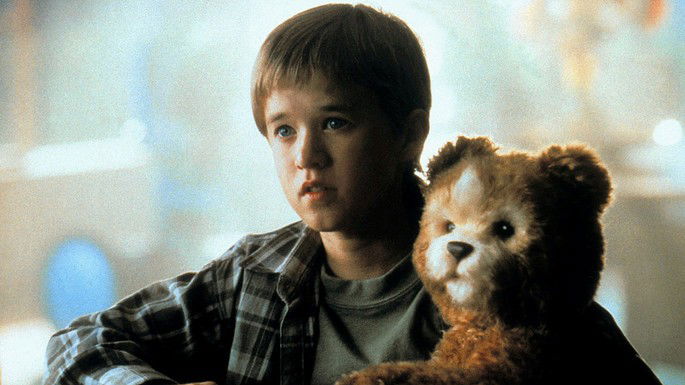 Garotinho com expressão triste segurando urso de pelúcia.