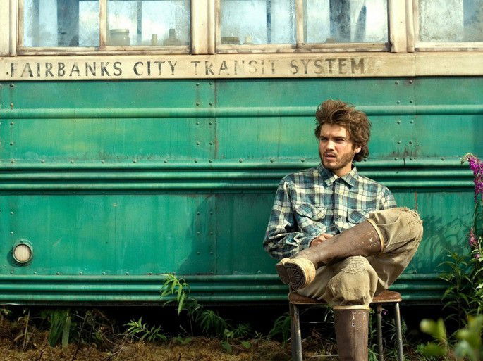 Homem sentado na frente de um onibus abandonado.