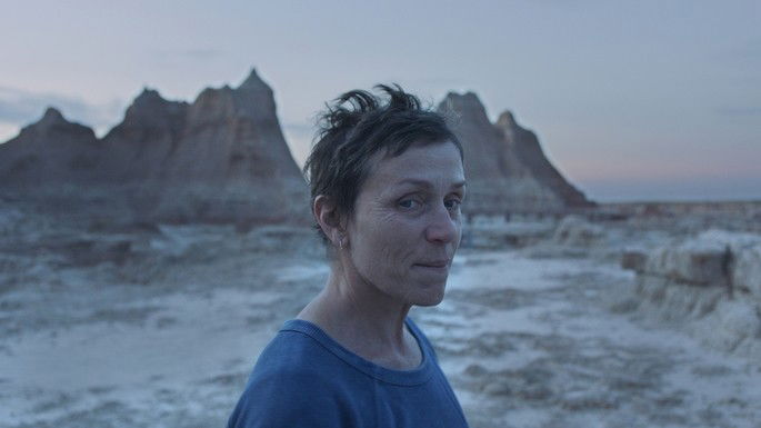 Mulher de cabelos curtos e blusa azul, com deserto e montanhas ao fundo