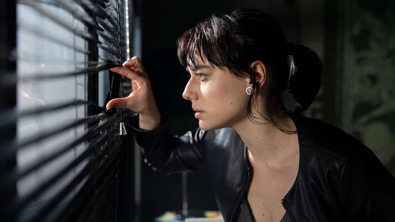 Mulher olhando pelo estore de uma janela.