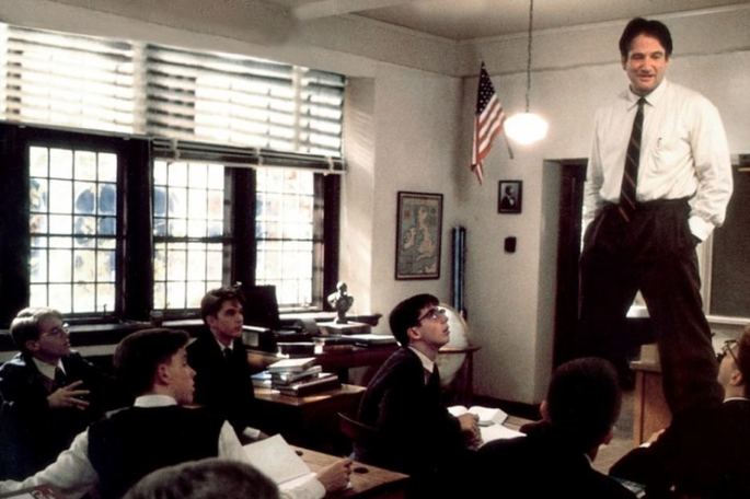 Professor dando aula de pé, em cima da mesa.