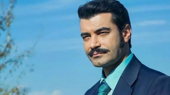 Homem elegante, de bigode, com expressão enigmática.