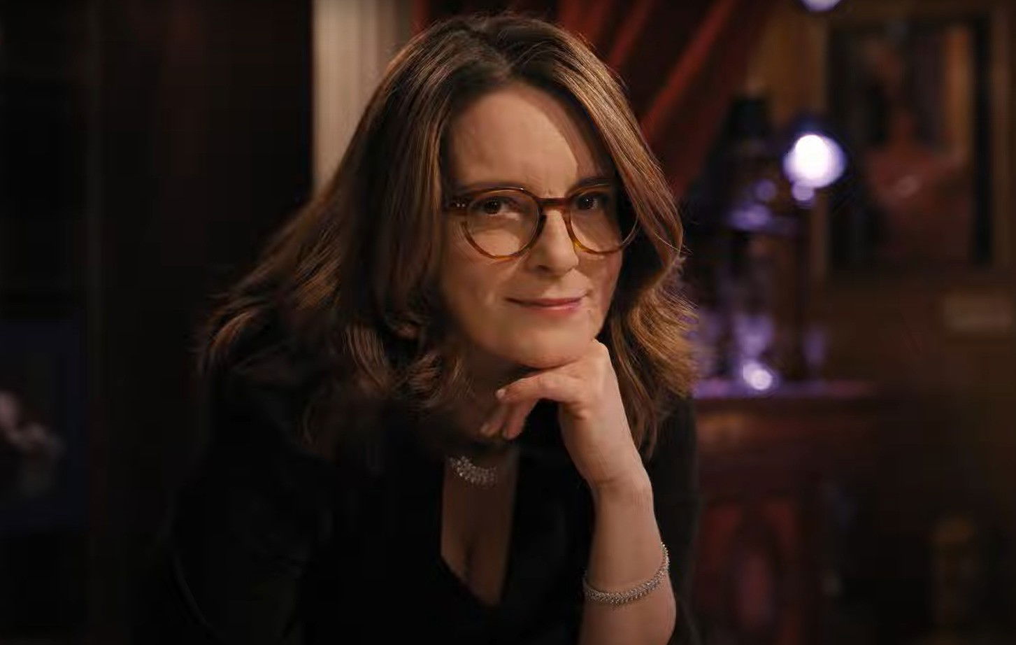 Comediante tina fey de cabelo jogado para o lado, óculos de grau, coloca a  mão sob o queixo